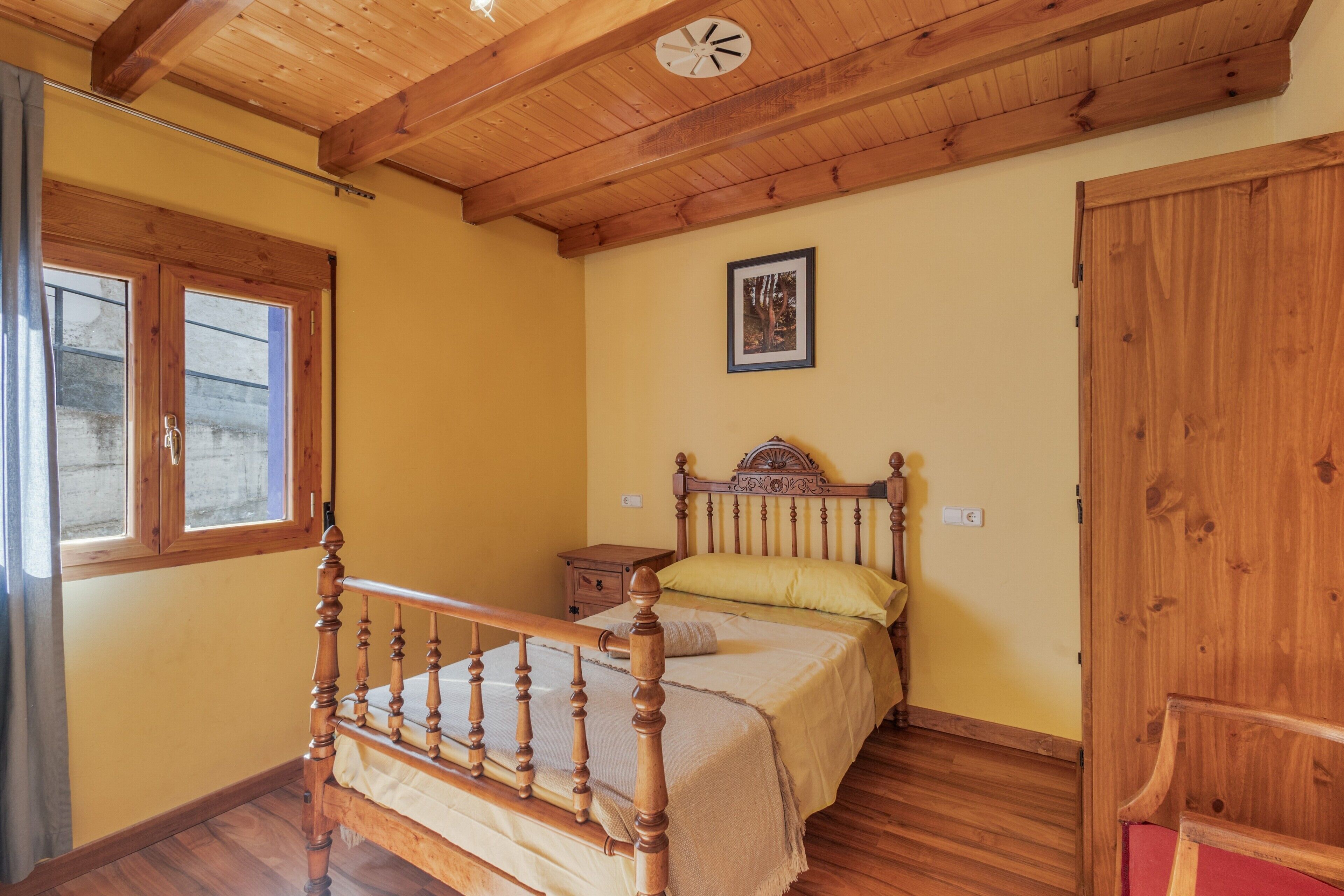 A bedroom with a wooden bed, a nightstand, a wall clock, a framed picture, and a door.