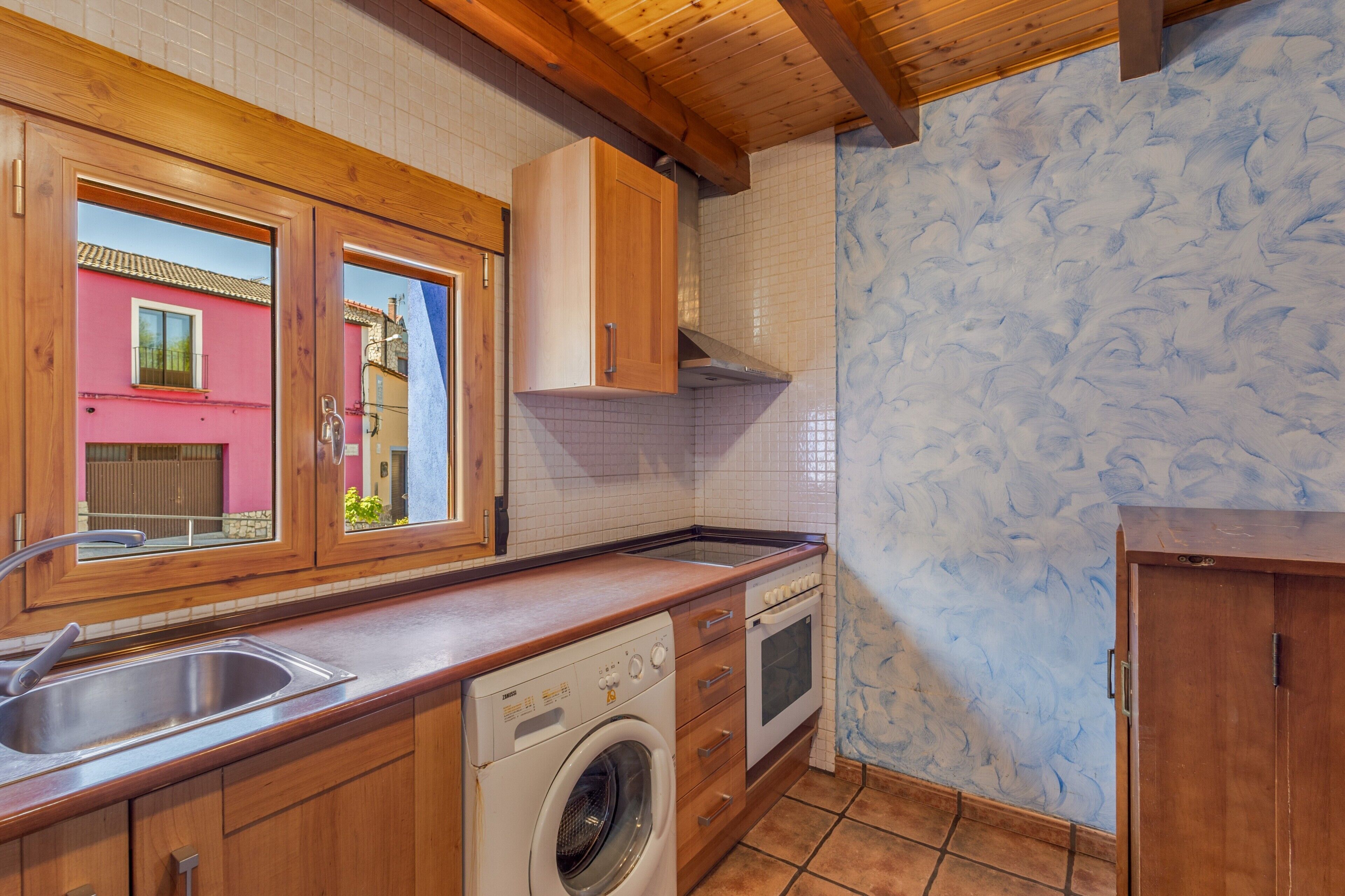 Eine Küche mit Holzausstattung, einer Waschmaschine und Blick durch ein Fenster.