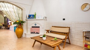 Une pièce avec une table en bois, un canapé, un grand vase rempli de fleurs, une cheminée et une horloge au mur.