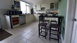 Cocina moderna con armarios blancos, lavavajillas, microondas y pileta. Hay tres taburetes y una ventana que proporciona luz natural.