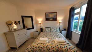 Un dormitorio con una cama, un aparador, un espejo, dos lámparas de noche y una ventana con cortinas.