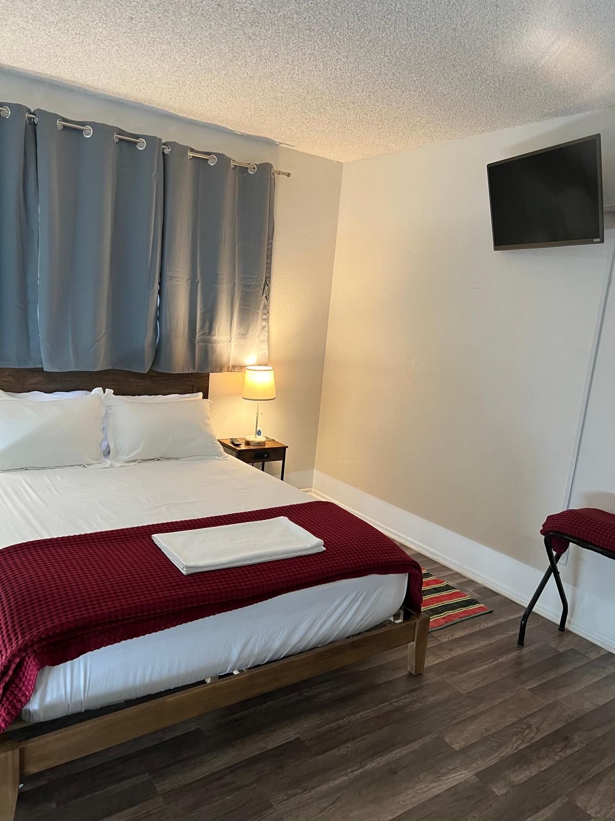 A hotel room with a bed, a nightstand, a lamp, a TV, and a red chair.