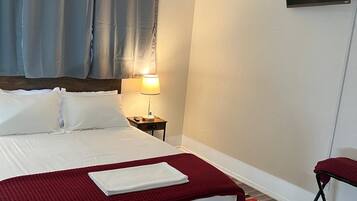 A hotel room with a bed, a nightstand, a lamp, a TV, and a red chair.