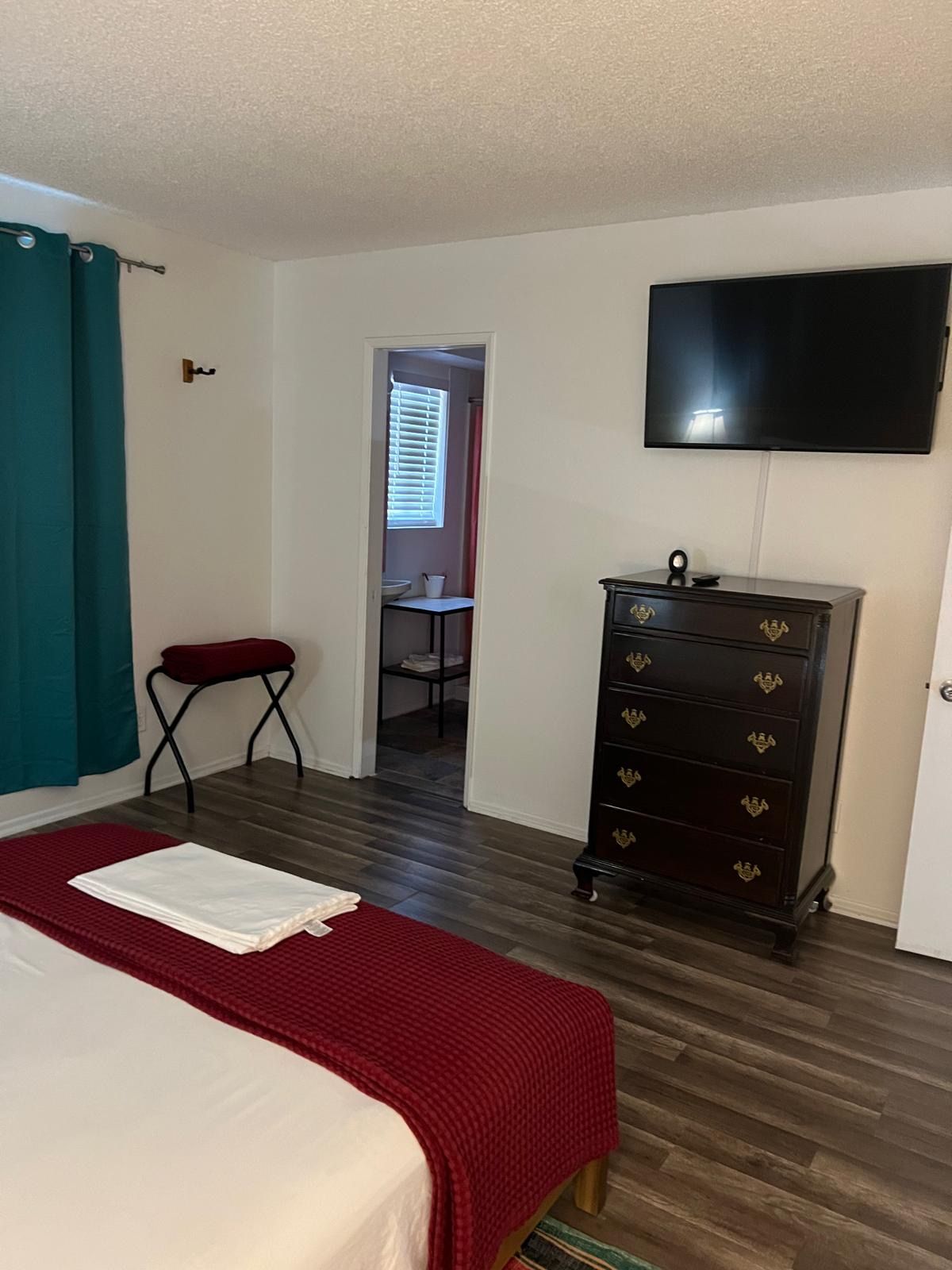 A hotel room with a bed, a dresser, a television, and a bathroom visible through an open door.