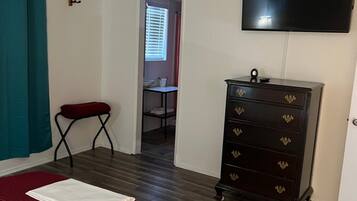 A hotel room with a bed, a dresser, a television, and a bathroom visible through an open door.