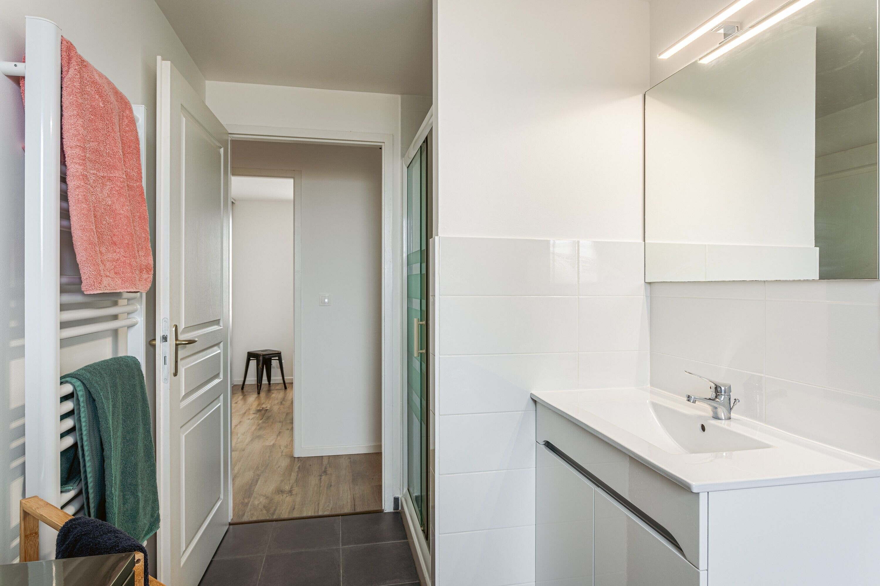 A modern bathroom with a white sink, a mirror, and a towel rack with towels.
