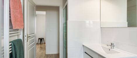 A modern bathroom with a white sink, a mirror, and a towel rack with towels.