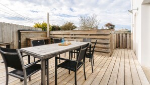 Une terrasse extérieure avec une plateforme en bois, une table et des chaises, et une clôture en bois en arrière-plan.
