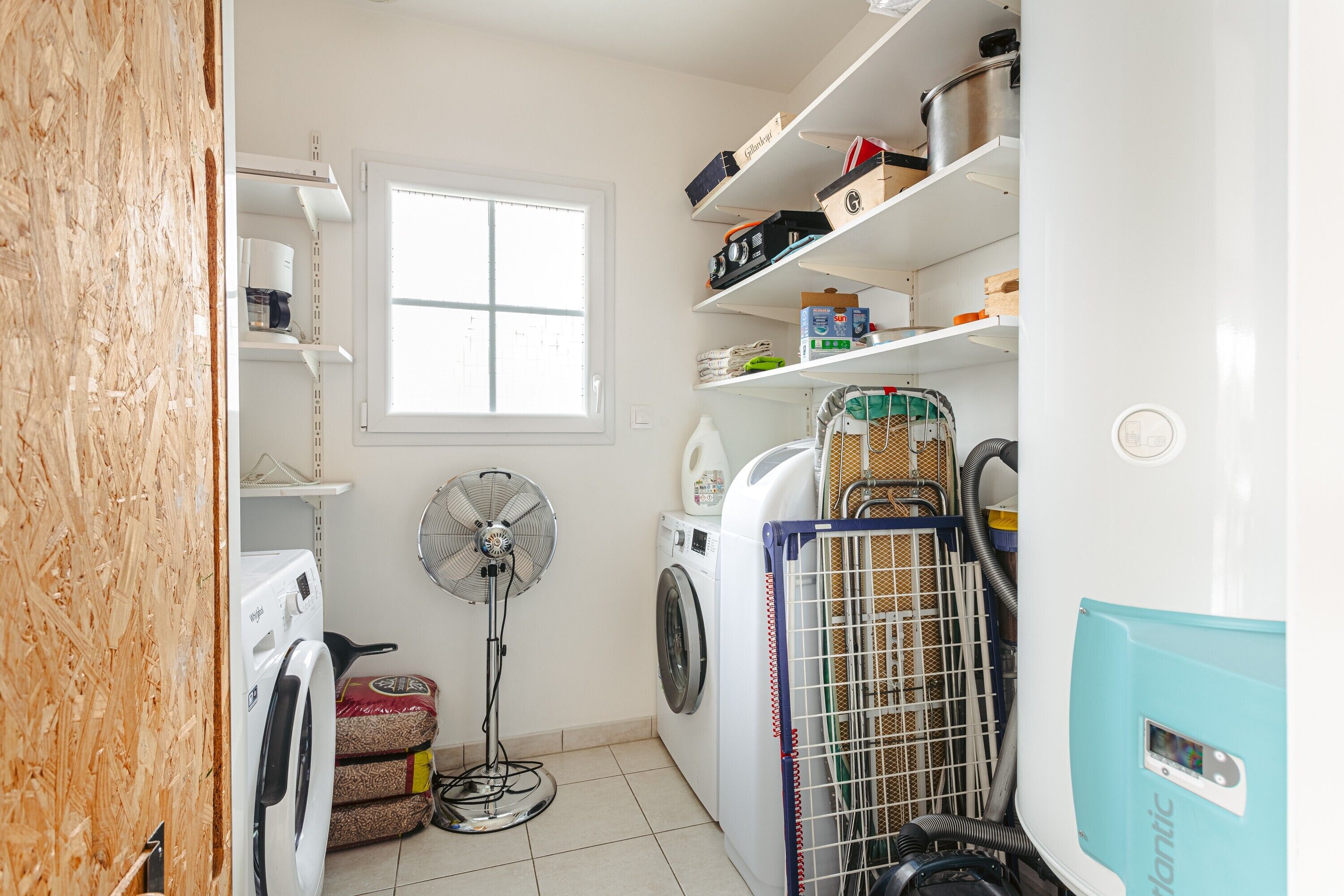 Un lavadero con lavadora, secadora, ventilador y cestas de ropa apiladas.