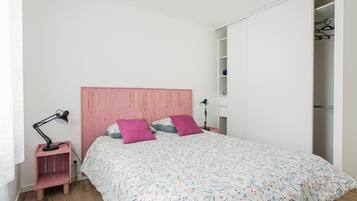 Een slaapkamer met een bed, een roze hoofdbord, twee roze kussens, een bedlampje en een garderobe.