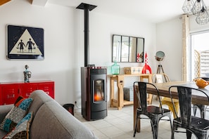 Un salon comprenant un canapé, un buffet rouge, un poêle en bois noir, une table à manger avec des chaises et un miroir accroché au mur.
