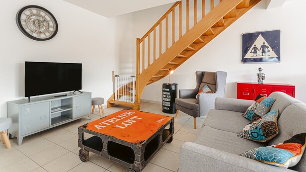 Un salon comprenant un téléviseur, un canapé, une table basse, un escalier et un meuble rouge.