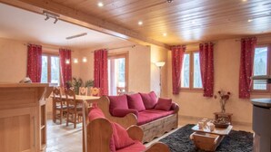 A cozy room with a wooden ceiling, a sofa, a dining table, and a fireplace. - Apartment 'La Grange - 4 Pers' with Mountain View, Private Garden and Wi-Fi (Taninges)