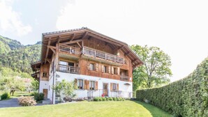 A two-story wooden chalet with balconies, a white exterior, and a mountainous backdrop. - Apartment 'La Grange - 4 Pers' with Mountain View, Private Garden and Wi-Fi (Taninges)