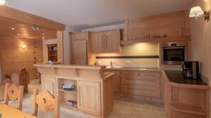A kitchen with wooden cabinets, a central island, a built-in oven, and a coffee machine. - Apartment 'La Grange - 4 Pers' with Mountain View, Private Garden and Wi-Fi (Taninges)