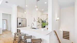 Uma cozinha moderna com ilha central, banquetas, eletrodomésticos de aço inoxidável e iluminação pendente.