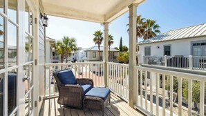 A covered porch with wicker furniture, a white railing, and a view of neighboring houses and palm trees.