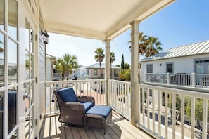 A covered porch with wicker furniture, a white railing, and a view of neighboring houses and palm trees.