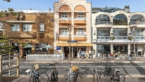 Una calle con una hilera de edificios, incluyendo una construcción de dos pisos con balcón y un edificio moderno con fachada de vidrio.