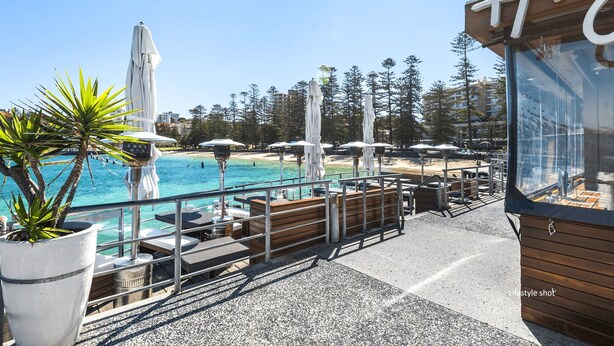 Una terraza frente al mar con mesas al aire libre, sombrillas y una piscina.