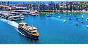 Un ferry con diseño blanco y amarillo, atracado en un muelle con un paisaje urbano al fondo.