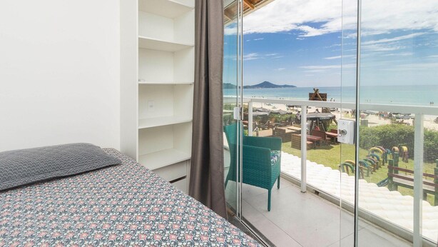 A balcony with a view of the beach and a chair. - Apartamento Espetacular em Bombinhas (Bombinhas)