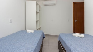 A small, clean room with two single beds, a wooden door, and a white air conditioning unit on the wall. - Apartamento Espetacular em Bombinhas (Bombinhas)