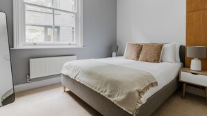 A bedroom with a bed, a nightstand, a lamp, a window, and a radiator. - Blueground | Clerkenwell, near Moorgate & tube (London)