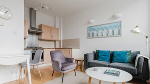 A modern living room with a grey sofa, a small round coffee table, and a grey armchair. There is a kitchen area with wooden cabinets and a stove. - Blueground | Clerkenwell, near Moorgate & tube (London)