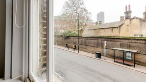 A view from a window overlooking a street with a brick wall, a bus stop, and buildings in the background. - Blueground | Clerkenwell, near Moorgate & tube (London)