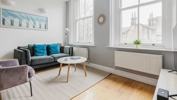 A modern living room with a grey sofa, a round coffee table, and a view of buildings through large windows. - Blueground | Clerkenwell, near Moorgate & tube (London)