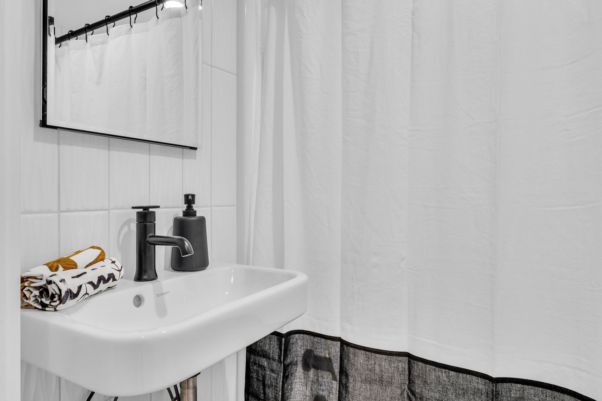 A bathroom with a white sink, black faucet, and a towel with a white and orange pattern.