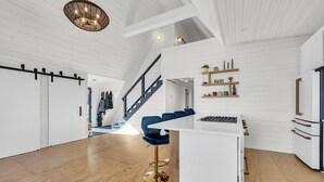 Una cocina moderna con armarios blancos, una isla central y un taburete azul.