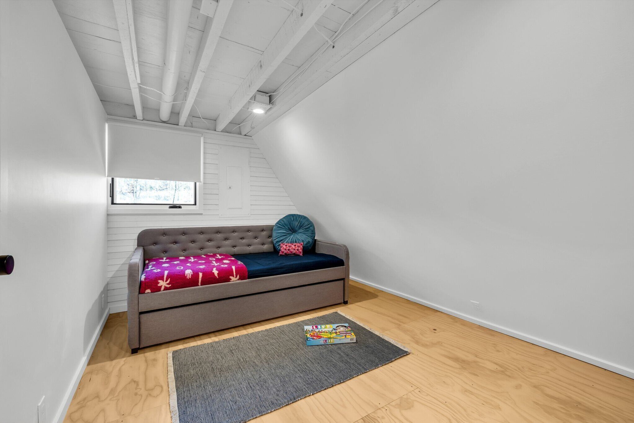 Ett litet, väl upplyst rum med en grå soffa, ett fönster och ett trägolv.