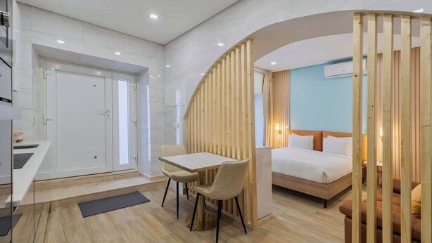 A modern hotel room with a wooden partition, a bed, a desk with a chair, and a small kitchenette. - Canto Doce Troino (Setúbal)