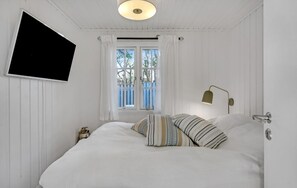 A bedroom with a bed, a window with curtains, a wall-mounted TV, and a bedside lamp. - Lovely summer house by Arresø (Hillerød)