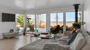 A spacious living room with a large sofa, a fireplace, and a view of the outdoors. - Lovely summer house by Arresø (Hillerød)