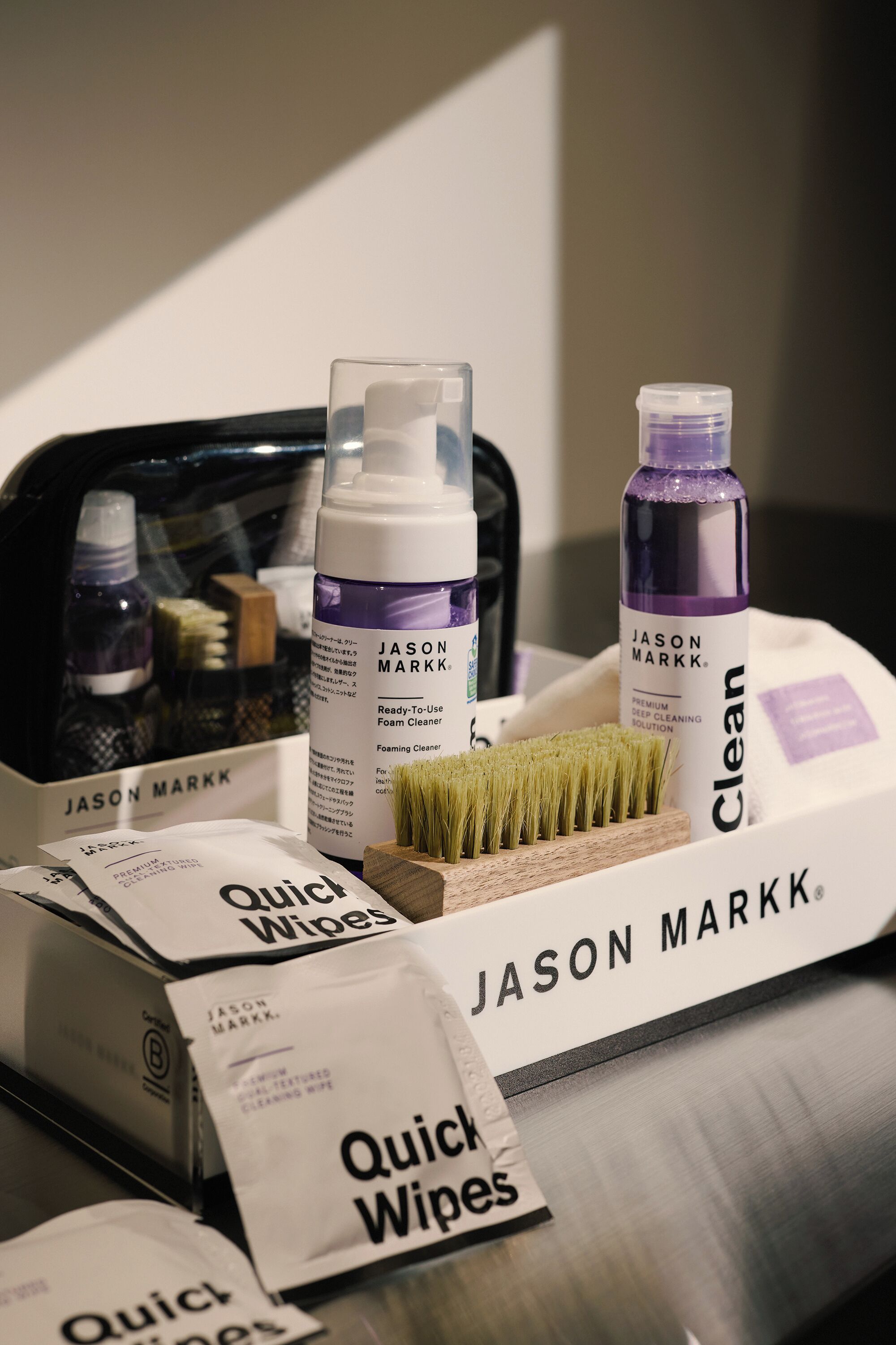 A collection of Jason Markk cleaning products, including a foam cleaner, a brush, and quick wipes, arranged on a table.