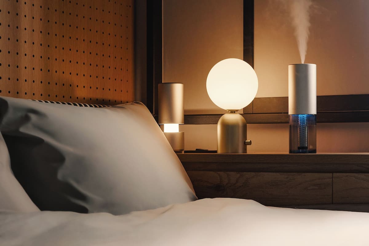 Een net opgemaakt bed met een kussen, een aan de muur bevestigde lamp en een waterornament dat stoom uitstoot.