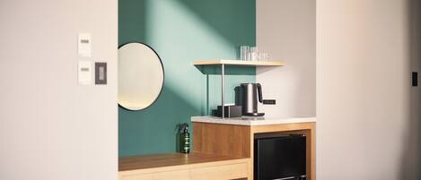 A compact kitchenette with a coffee maker, a small refrigerator, and a shelf with glasses.