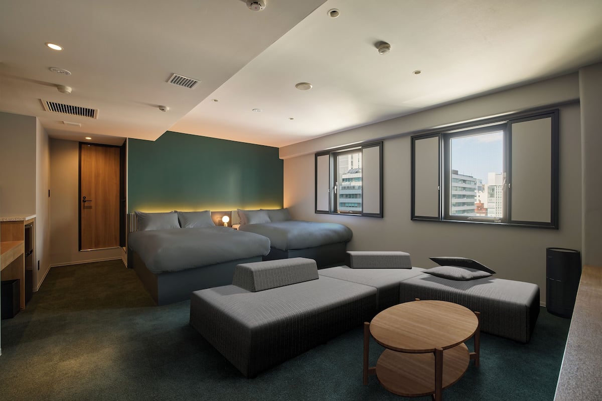 Een moderne hotelkamer met een groot bed, een slaapbank, een tafeltje en uitzicht op de stad door grote ramen.