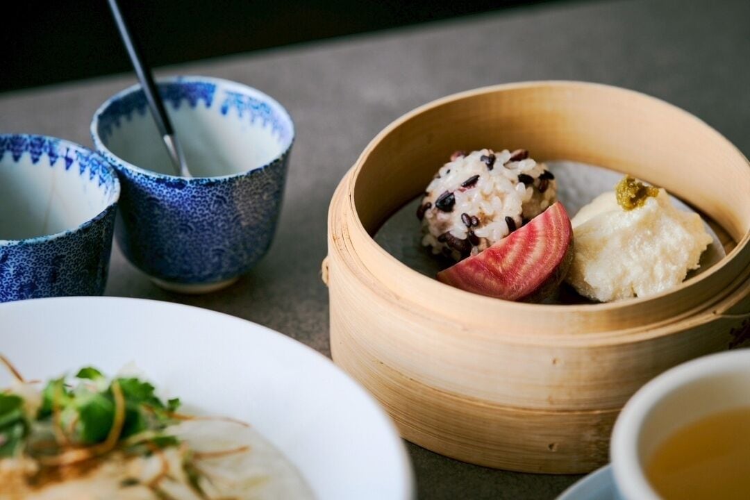 Une table garnie de différents plats, notamment un panier à vapeur en bambou contenant des raviolis et un bol de soupe.