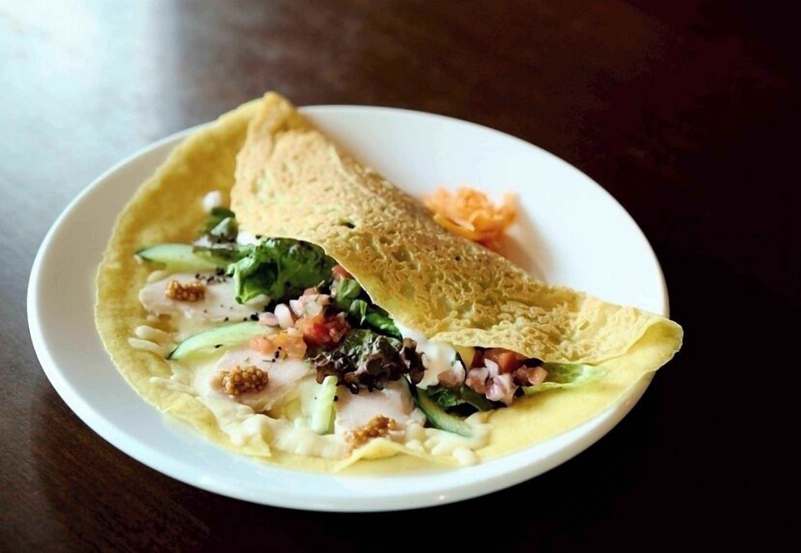 A plate with a folded crepe containing vegetables and a sauce.