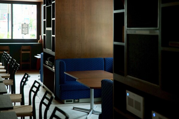 Interior de un restaurante con una zona de mesas en azul, una pared de madera y una ventana con vistas al exterior.