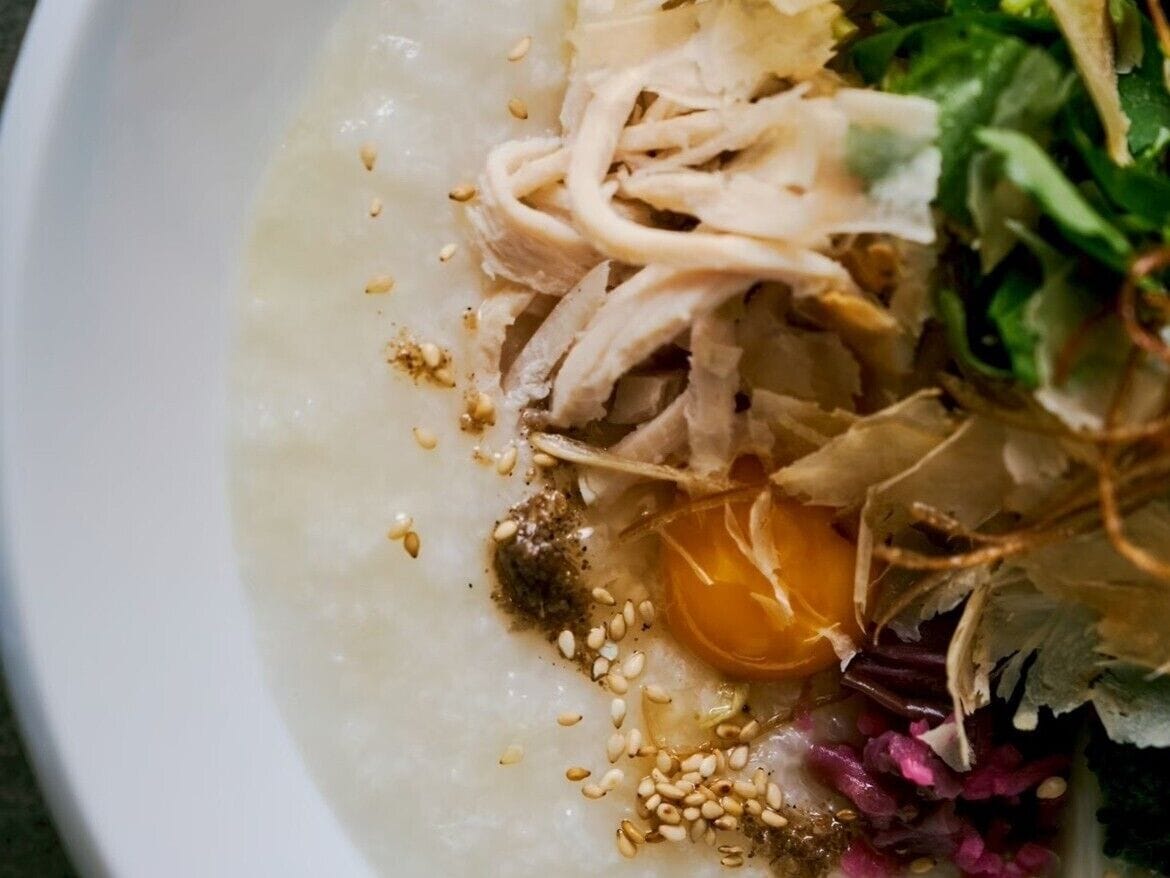 Un bol contenant des aliments, notamment du poulet effiloché, des graines de sésame et des légumes verts.