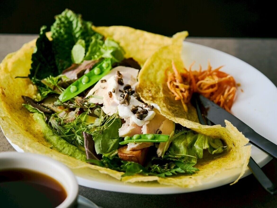 A plate with a wrap containing greens, a poached egg, and a side of shredded carrots.