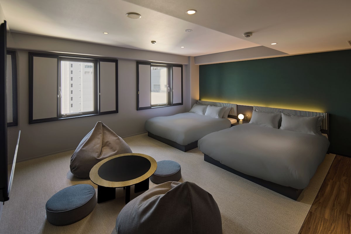 Een moderne hotelkamer met twee bedden, een bank, een kleine tafel en uitzicht op de stad door grote ramen.