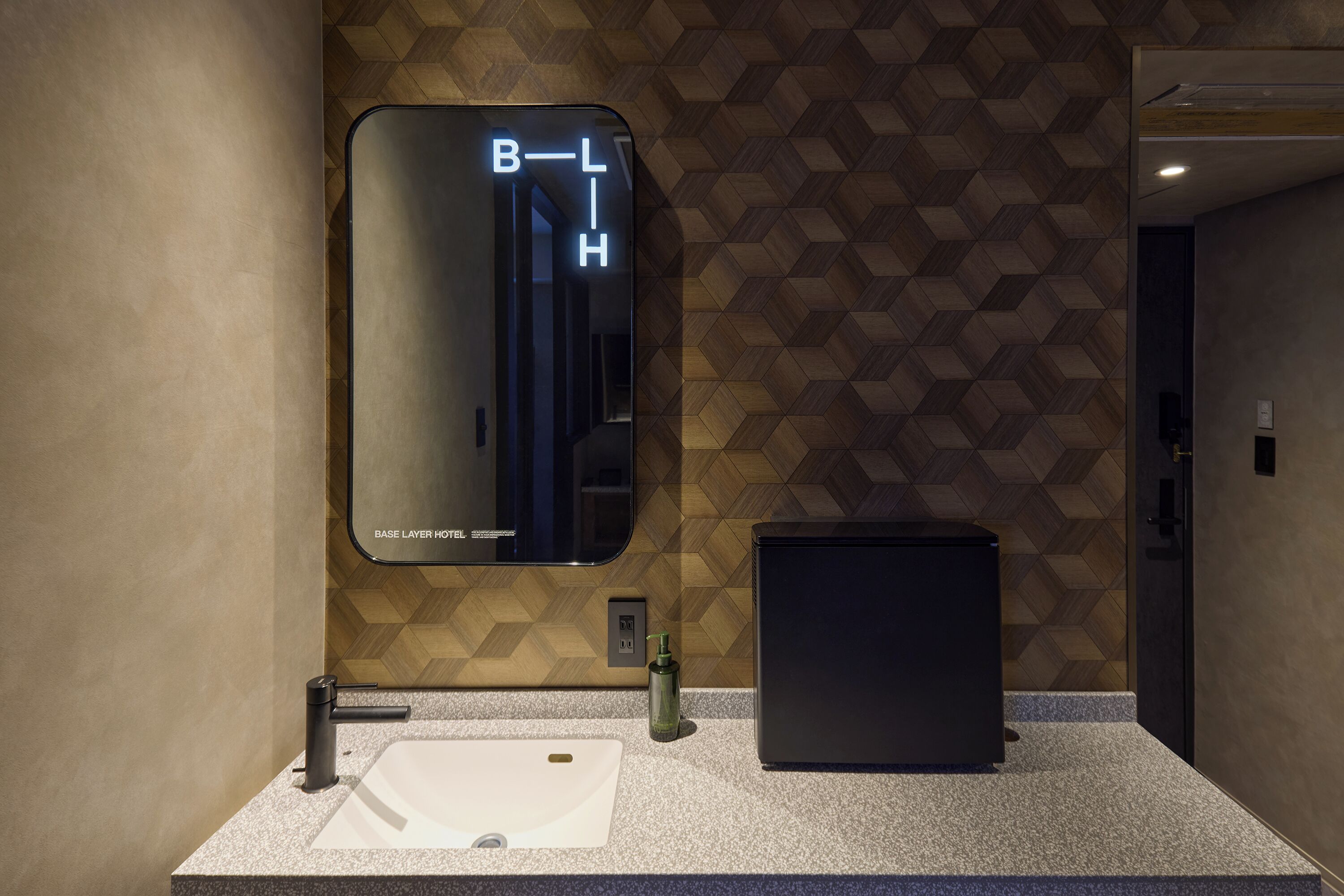 Un baño moderno con un revestimiento de pared de diseño geométrico, un espejo grande, un lavabo y un mueble negro.