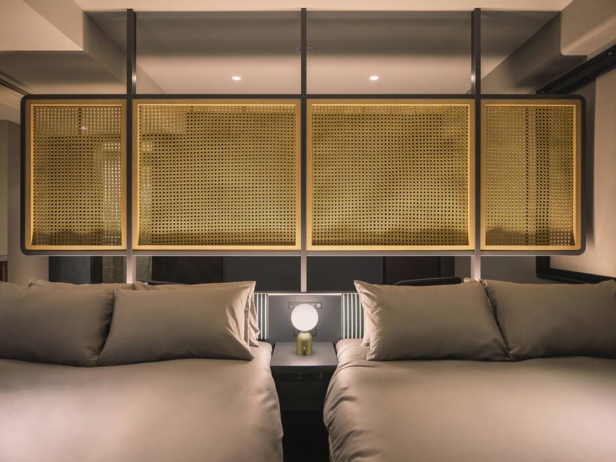 Una habitación de hotel moderna con una cama grande, una mesita de noche y un separador decorativo con una lámpara circular.