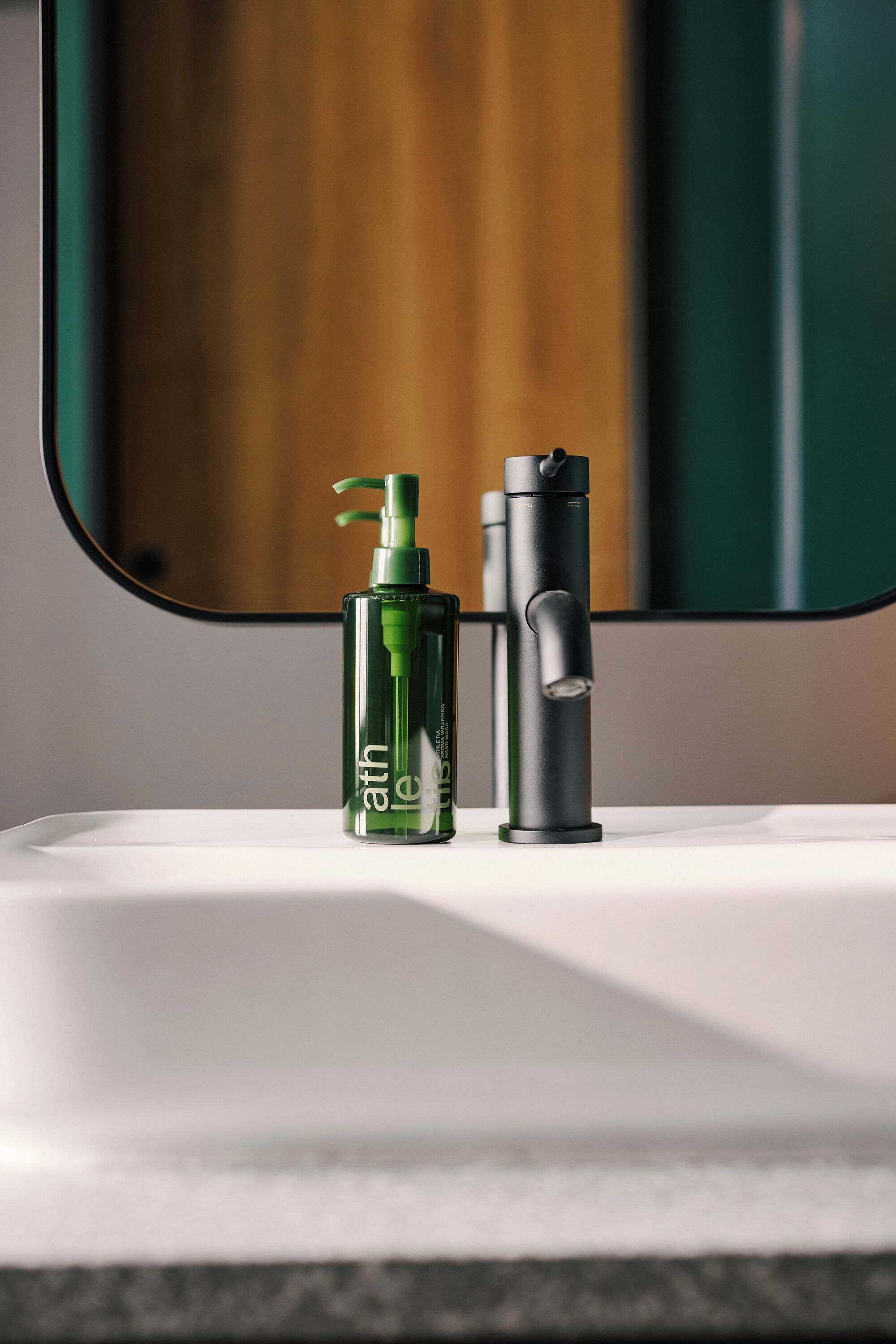 A bathroom with a white sink, a green bottle of lotion, and a black faucet.